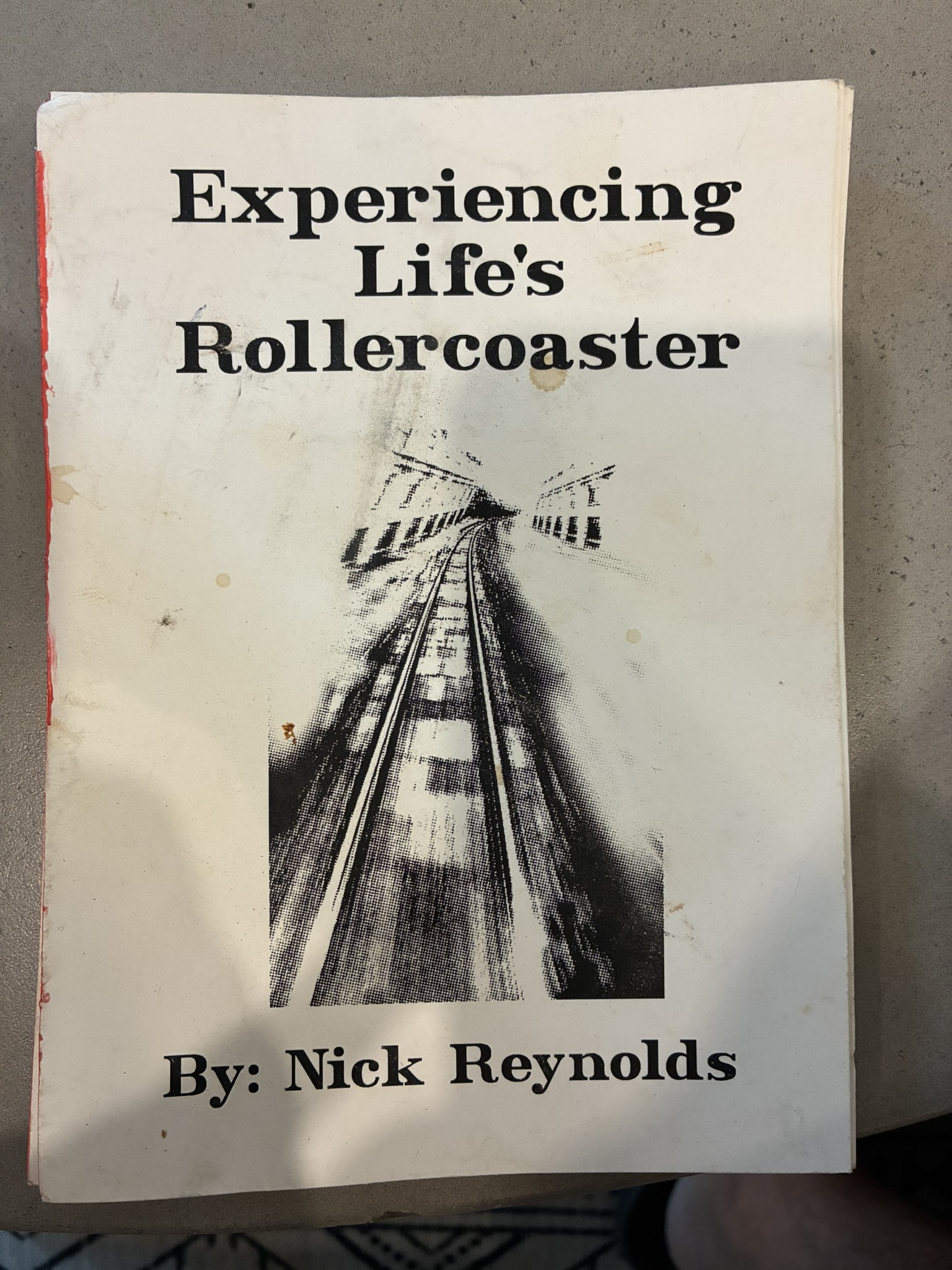 Cover of the bound manuscript Experiencing Life's Rollercoaster by Nick Reynolds, showing a halftone photograph looking up a wooden rollercoaster track above the printed byline.